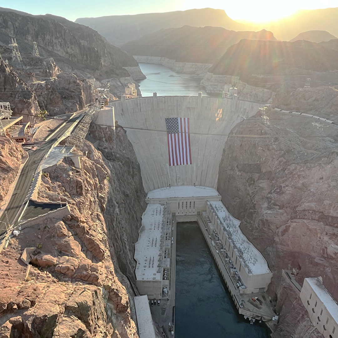 Hoover Dam at golden hour, the American flag draped down its concrete face